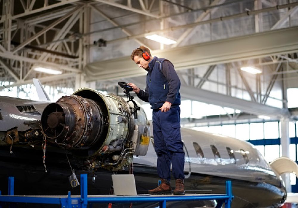 Aircraft engineer in the hangar repairing and maintaining airplane jet engine.